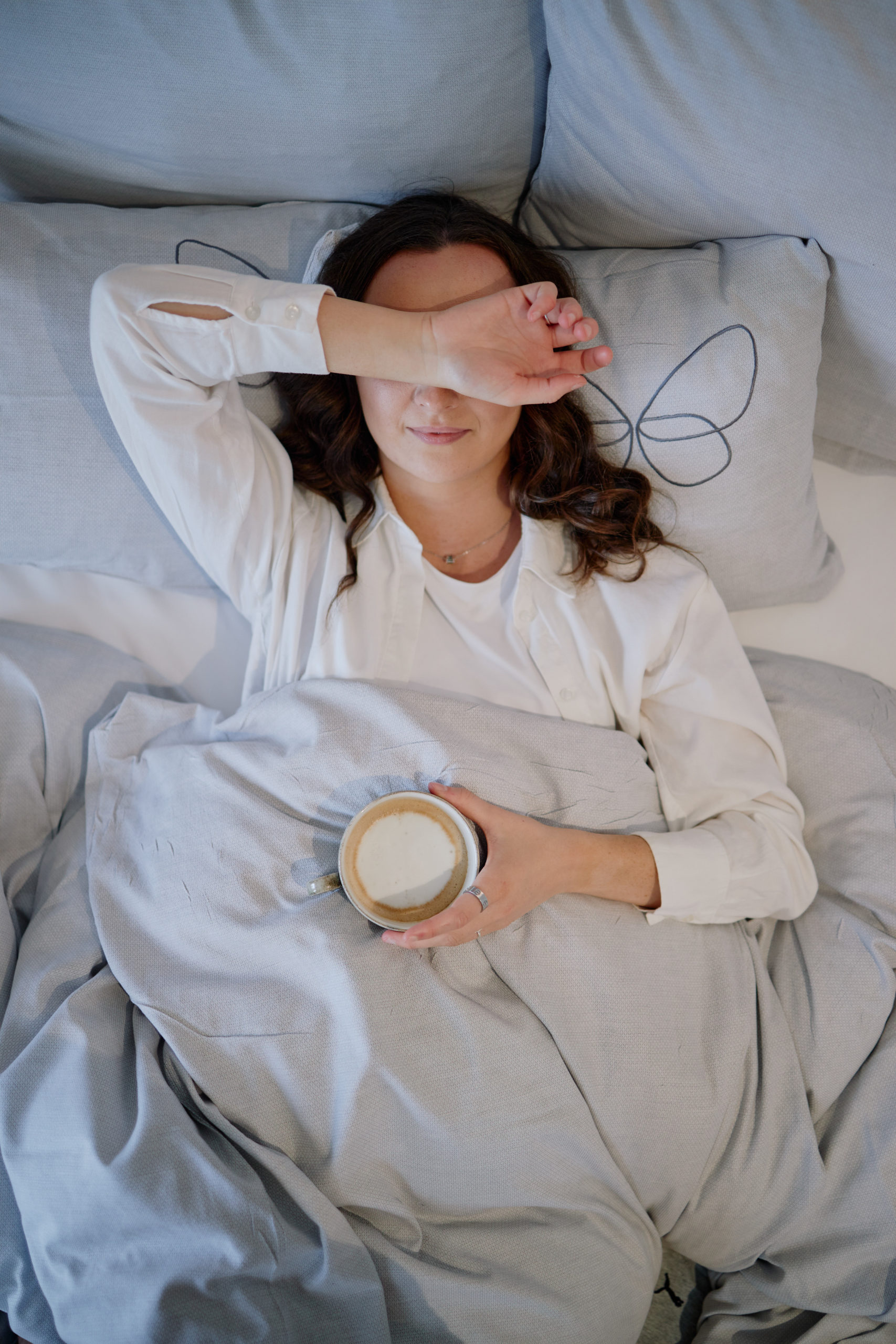 Eine Frau liegt mit einer Tasse Kaffee in einem Bett